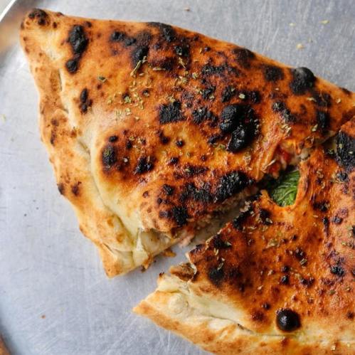 A golden-brown calzone with a crispy crust, showing hints of herbs and a filling peeking out.