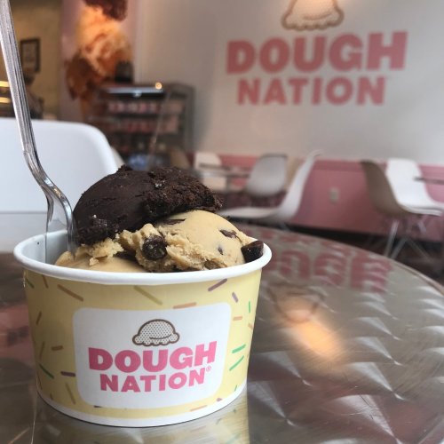 A cup of cookie dough ice cream with a spoon, set against a pink and white café backdrop.