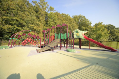 Colorful playground equipment with slides and climbing structures, surrounded by trees and a clear blue sky.