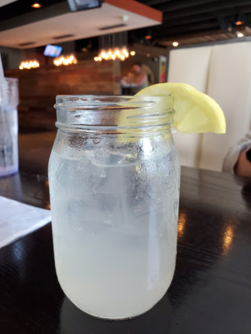 A mason jar filled with lemonade, garnished with a lemon slice, on a dark wooden table.