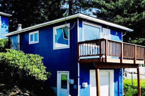 A blue two-story house with a wooden deck, surrounded by greenery and trees.