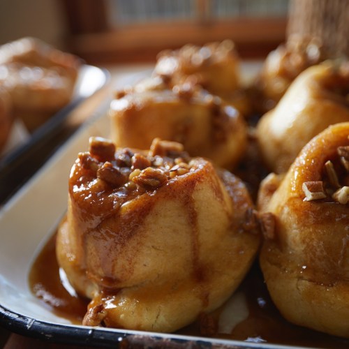 Close-up of warm, caramel-drizzled cinnamon rolls topped with chopped pecans on a white plate.