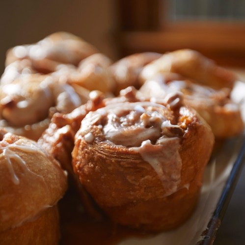 A close-up of freshly baked cinnamon rolls drizzled with icing, arranged on a plate.
