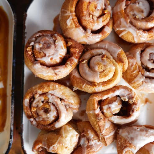A close-up of freshly baked cinnamon rolls drizzled with icing, arranged on a white platter.