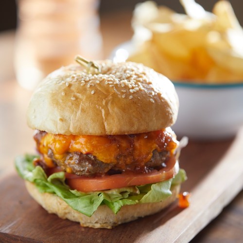 A juicy cheeseburger with lettuce, tomato, and a sesame seed bun, served with a side of potato chips.