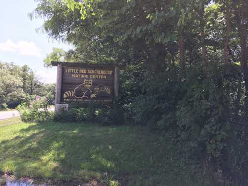 Sign for Little Red Schoolhouse Nature Center surrounded by greenery, with a raccoon illustration.