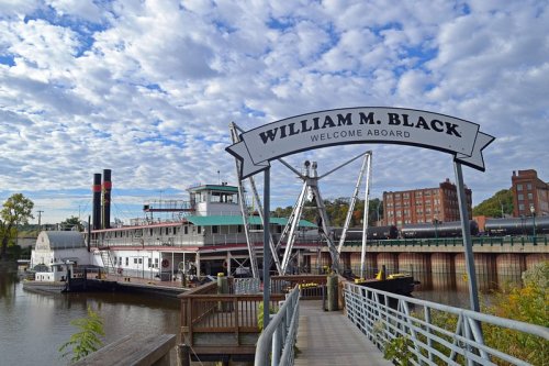 A riverboat named "William M. Black" docked at a pier, with a cloudy sky and buildings in the background.