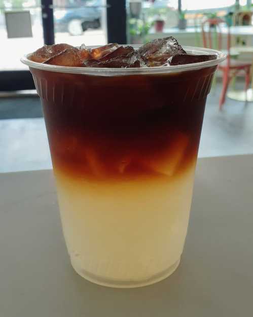 A clear cup filled with iced coffee, featuring a gradient from dark brown at the top to light beige at the bottom.