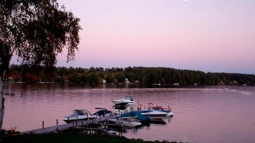 Serene lake at sunset with boats docked and a pastel sky reflecting on the water.