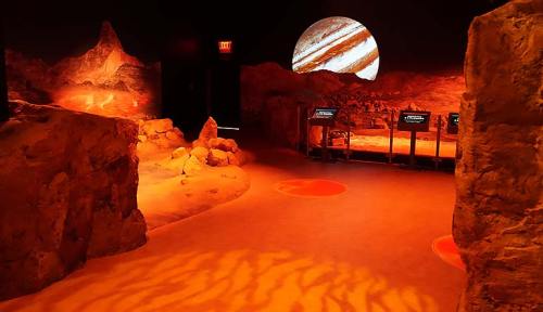 A dimly lit exhibit simulating a rocky, alien landscape with a large planet projection on the wall.