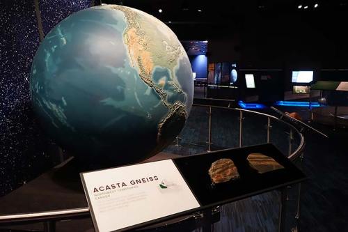 A large globe depicting Earth, with a display about Acasta Gneiss rock formation in a museum setting.
