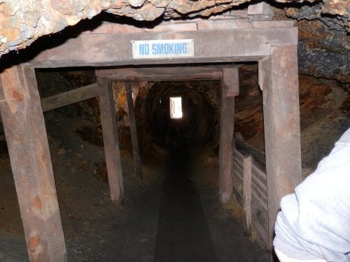 A dimly lit mine tunnel with wooden supports and a "No Smoking" sign at the entrance.