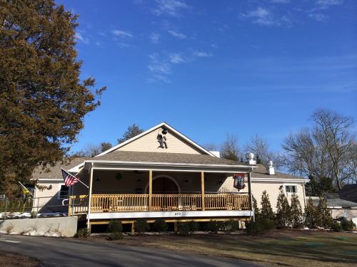 A light-colored house with a porch, American flag, and trees under a clear blue sky.