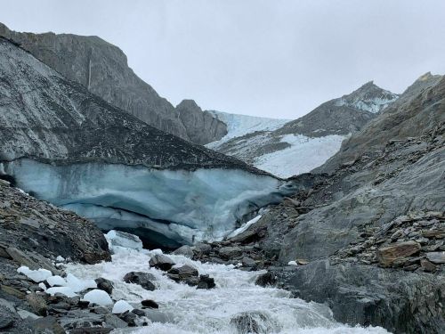 A glacial landscape with icy blue formations, rocky terrain, and a rushing river flowing through the valley.