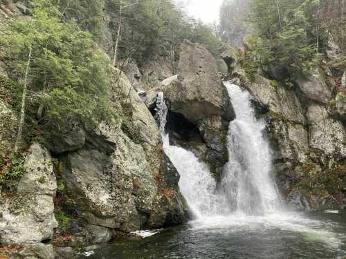 A scenic waterfall cascading over rocky cliffs, surrounded by lush greenery and misty mountains in the background.