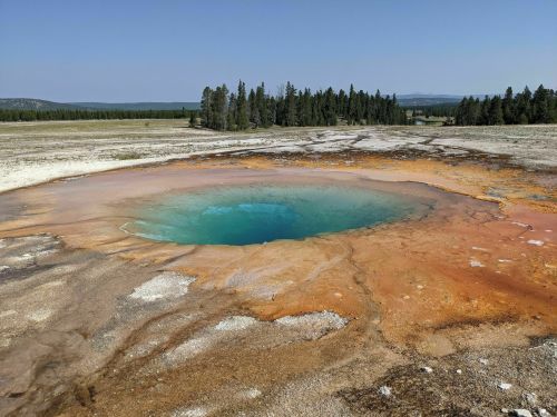 A vibrant geothermal hot spring with turquoise water surrounded by orange and yellow mineral deposits in a natural landscape.