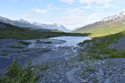 A serene landscape featuring a calm lake surrounded by rocky terrain and snow-capped mountains under a clear sky.