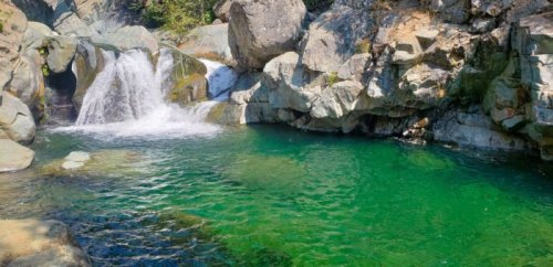 A serene natural pool with clear green water and a small waterfall surrounded by rocky terrain.