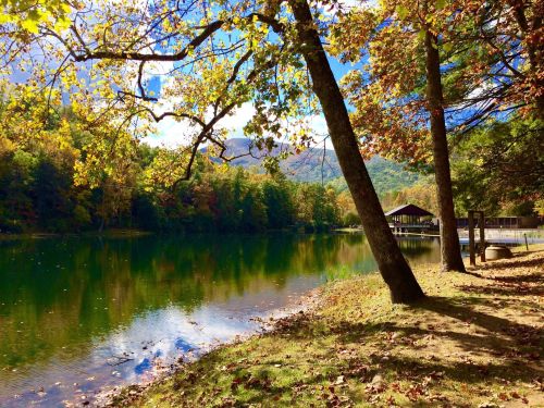 A serene lake surrounded by colorful autumn trees and a wooden pavilion, reflecting the vibrant landscape.
