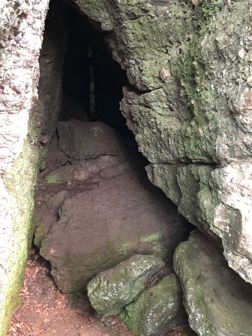 A dark cave entrance surrounded by rocky terrain and moss-covered stones.