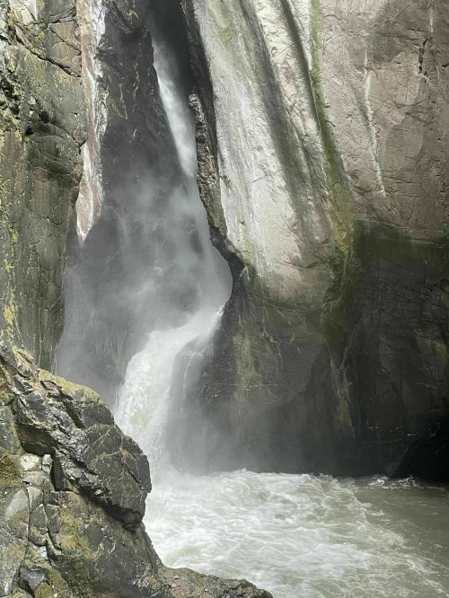A waterfall cascading down rocky cliffs, surrounded by mist and lush greenery.