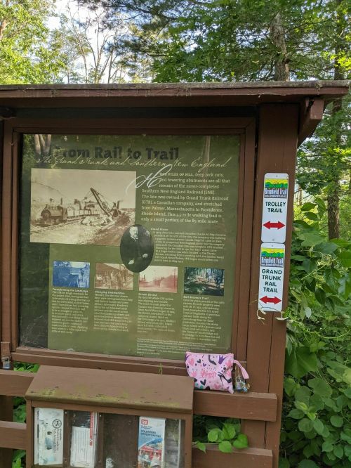 Information sign about the Iron Rail to Trail, featuring historical photos and trail directions in a wooded area.