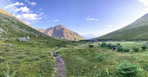 A panoramic view of a lush green valley surrounded by mountains under a clear blue sky.