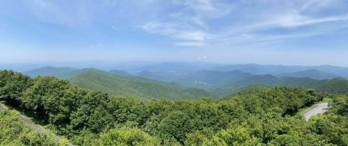 A panoramic view of lush green mountains under a clear blue sky, with rolling hills in the distance.