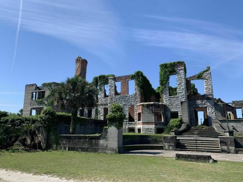 Ruins of a stone building overgrown with greenery, set against a clear blue sky.