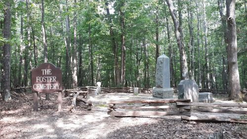 A wooded area featuring a sign that reads "The Foster Cemetery" and several gravestones surrounded by a wooden fence.