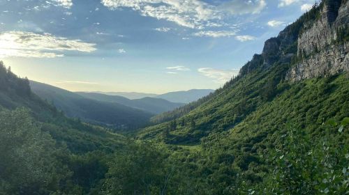 A serene valley surrounded by mountains, with lush greenery and a clear sky at sunset.