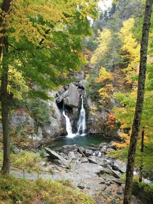 A serene waterfall cascades into a pool, surrounded by vibrant autumn foliage and rocky terrain.