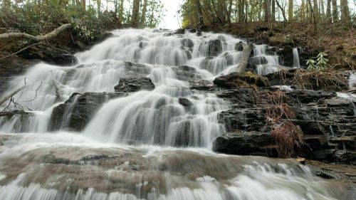 A cascading waterfall flows over rocky terrain, surrounded by lush greenery and trees.