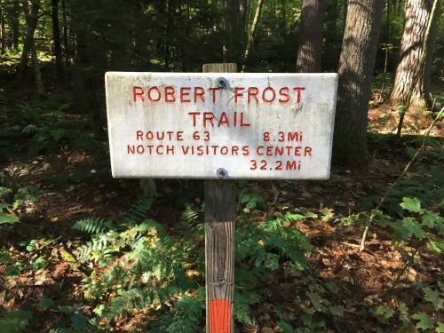 Sign for Robert Frost Trail, indicating Route 63, 8.3 miles to Notch Visitors Center, 32.2 miles total. Surrounded by trees.