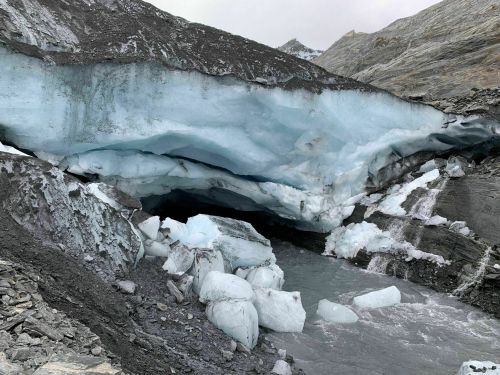 A glacier with blue ice formations and rocky terrain, partially melting into a river below.
