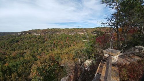 A panoramic view of a lush, green valley with autumn foliage and rocky cliffs under a clear blue sky.