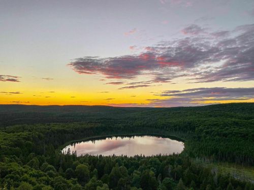 A serene landscape featuring a circular lake surrounded by lush green trees, under a colorful sunset sky.