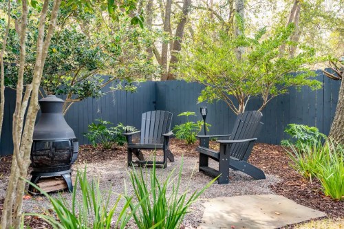 Cozy outdoor seating area with two black chairs, a fire pit, and lush greenery surrounded by a wooden fence.
