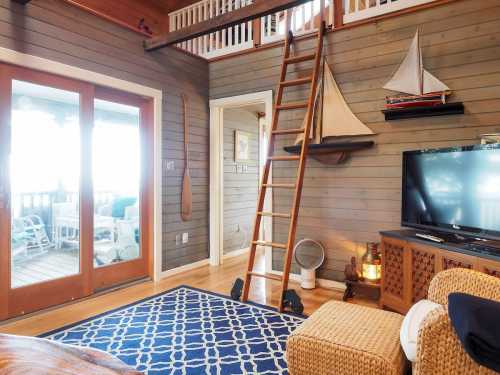 Cozy interior with wooden walls, a ladder to a loft, nautical decor, and a blue patterned rug. Bright natural light.