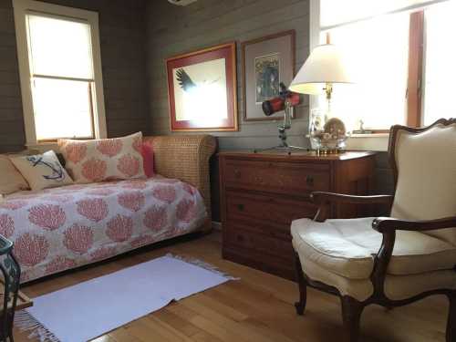 Cozy room featuring a daybed with coral-patterned cover, wooden dresser, and a vintage armchair by the window.