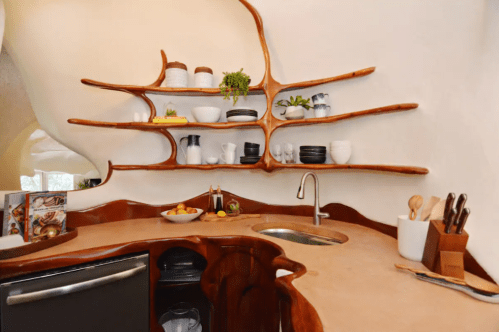 A unique kitchen with organic-shaped wooden shelves, a sink, and various dishes and utensils displayed.