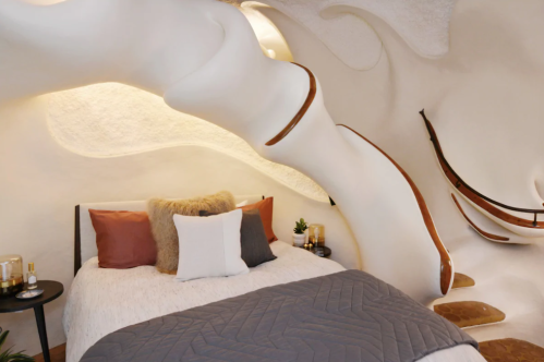 A cozy, modern bedroom with organic shapes, a plush bed, and warm lighting, featuring unique architectural details.