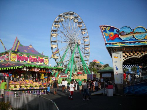 A vibrant carnival scene featuring a Ferris wheel, colorful game booths, and visitors enjoying the festivities.