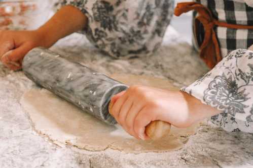 A person rolls out dough with a marble rolling pin on a countertop, wearing a patterned shirt.