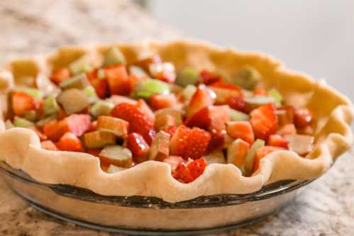 A freshly made pie filled with chopped strawberries and rhubarb in a golden crust, resting on a marble countertop.