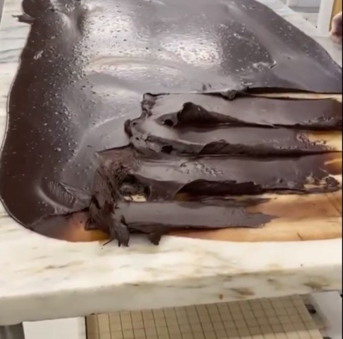 A smooth layer of melted chocolate spread across a marble surface, with some chocolate pooling at the edges.