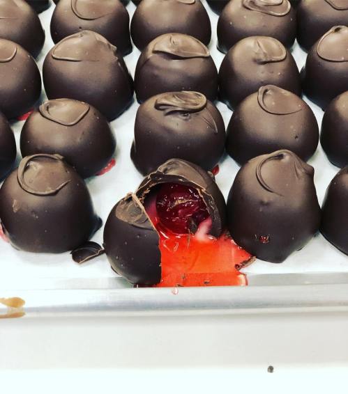 A tray of chocolate-covered candies, one with a cherry filling oozing out.