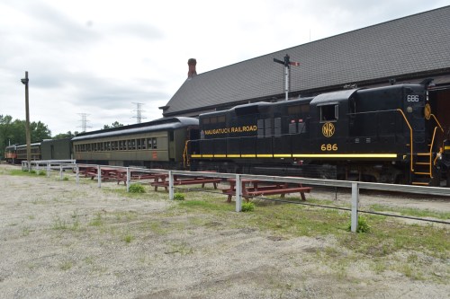 A black locomotive with the number 686 parked beside a vintage passenger car at a train station.