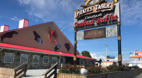 Sign for "Pirate's Table Calabash Seafood Buffet" outside a rustic building with crab decorations and a blue sky.