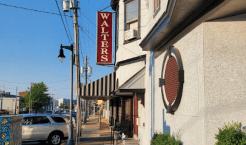 A street view of a building with a sign reading "WALTERS," featuring a clear blue sky and parked cars.